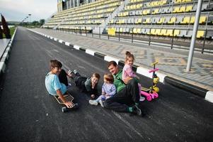 vier kinderen met vader in asfalt spelen en plezier hebben. sportfamilie brengt vrije tijd buitenshuis door met scooters en skates. foto