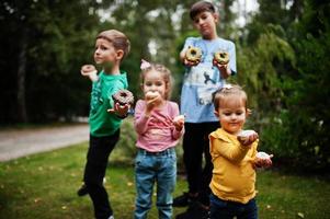 vier kinderen met donuts op de avondtuin. lekker lekker donut eten. foto