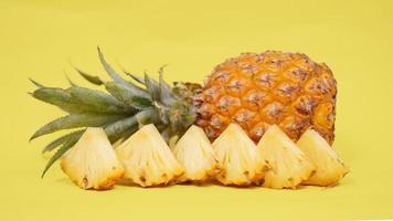 ananasfruit en sommige van zijn stukken geïsoleerd op een gele achtergrond foto