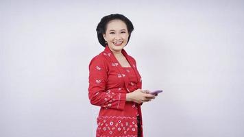 Aziatische schoonheid in kebaya grinnikt met smartphone geïsoleerd op witte achtergrond foto