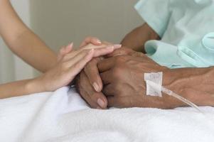 close-up van de bezoeker die de hand van de senior patiënt vasthoudt in het ziekenhuis, de gezondheidszorg en het medische concept foto