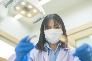 vrouwelijke tandarts met een tandheelkundige sonde en een spiegel die de patiënt in de tandheelkundige kliniek controleert, tandencontrole en gezond gebit concept foto