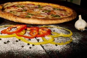 pepperoni pizza met ham en jalapeno chilipepers op oude houten tafel foto