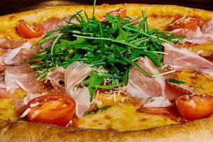 Italiaanse pizza met ham, tomaten en kruiden op een houten tafel foto