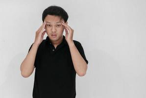 portret van een jonge aziatische man geïsoleerd op een grijze achtergrond die lijdt aan ernstige hoofdpijn, vingers naar de slapen drukken, ogen sluiten om pijn te verlichten met hulpeloze gezichtsuitdrukking foto