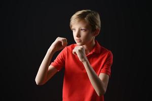 jongen in een rood t-shirt op een zwarte achtergrond houdt zijn handen in een beschermende pose foto