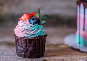 zelfgemaakte cupcakes met roze en turquoise crème, gedecoreerd met aardbeien en bosbessen foto