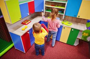 schattige zusjes spelen in indoor speelcentrum. kleuterschool of voorschoolse speelkamer. in de kinderkeuken. foto