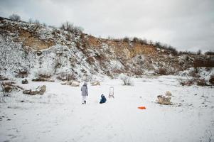 familie speelt en sleeën in de winter buiten, moeder en kinderen hebben plezier. foto