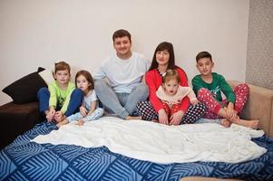 gelukkige grote familie heeft samen plezier in de slaapkamer. grote familie ochtend concept. vier kinderen met ouders dragen thuis een pyjama in bed. foto