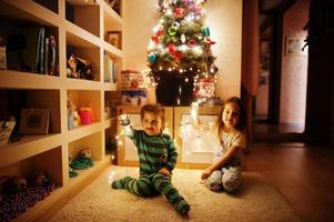 twee babymeisjeszusjes kijken naar de kerstboom met glanzende slingers op de avond naar huis. foto