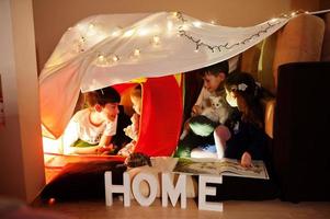 spelende kinderen met kitty in tent 's nachts thuis. hygge stemming. foto