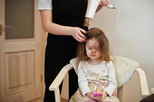 moeder met dochter die samen dagelijkse routine maakt. moeder borstelt en droogt het haar van het kind na het douchen. foto