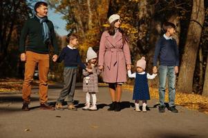 groot gezin met vier kinderen hand in hand en staan op de weg in het herfstpark. foto