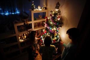 kinderen kijken op kerstboom met glanzende slingers op avond thuis. foto