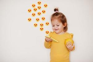 babymeisje in geel met citroen en mobiele telefoon met emoji van hartogen, geïsoleerde achtergrond. foto