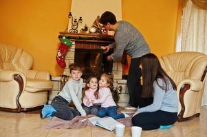 gelukkige jonge grote familie thuis bij een open haard in warme woonkamer op winterdag. foto