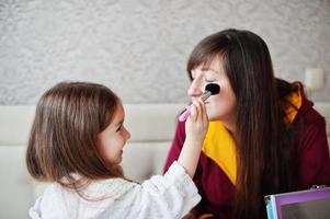 moeder en dochter doen make-up op het bed in de slaapkamer. foto