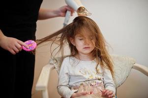 moeder met dochter die samen dagelijkse routine maakt. moeder borstelt en droogt het haar van het kind na het douchen. foto