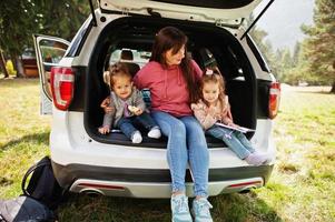 familie bij voertuiginterieur. moeder met haar dochters. kinderen in de kofferbak. reizen met de auto in de bergen, sfeerconcept. foto