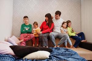 gelukkige grote familie heeft samen plezier in de slaapkamer. grote familie ochtend concept. vier kinderen met ouders dragen thuis een pyjama in bed. foto