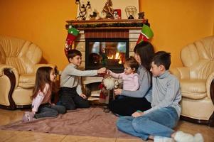 gelukkige jonge grote familie bij een open haard in warme woonkamer op winterdag. moeder met vier kinderen thuis. foto