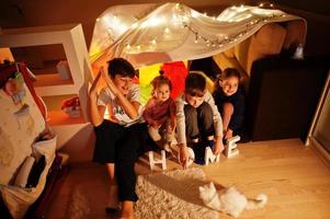 spelende kinderen met kitty in tent 's nachts thuis. hygge stemming. foto