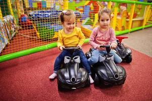 twee siters rijdt op een plastic auto in een indoor speelcentrum. foto