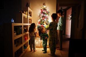 kinderen kijken op kerstboom met glanzende slingers op avond thuis. foto