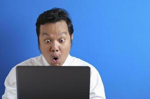 jonge aziatische zakenman die een casual wit overhemd draagt en naar een laptop kijkt, een verbaasde uitdrukking. foto