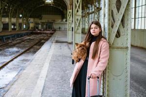 mooie jonge casual toeristenvrouw met hond en koffer die op trein wacht foto