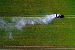 luchtfoto van tractor die pesticiden sproeit op groene haverveldopname vanuit drone foto
