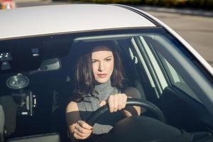 brunette vrouw die een witte auto bestuurt op een stedelijke achtergrond foto