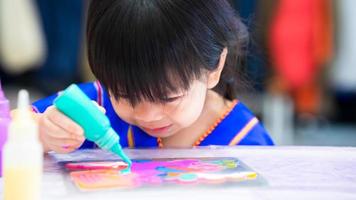 schattig meisje zit blauwe aquarelverf op roestvrijstalen plaat om een prachtig patroon te creëren. gelukkig kind met kunstwerken. foto