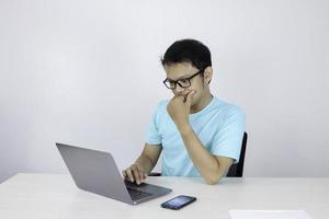 jonge aziatische man is serieus en concentreert zich bij het werken op een laptop op tafel. Indonesische man met een blauw shirt. foto