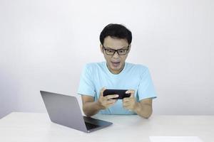 boze aziatische jongeman wordt boos op de smartphone wanneer hij een spel speelt op het werk. Indonesische man met een blauw shirt. foto