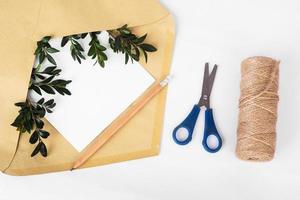 ambachtelijke papieren envelop met leeg papier en groene twijgen onder verfrommeld papier en bundelwikkeling op witte achtergrond foto
