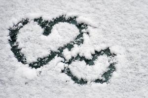 twee harten symbolen getekend in de witte sneeuw op de voorruit van een auto in de winter foto