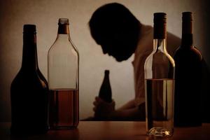 alcoholisme - silhouet van man achter alcoholflessen foto