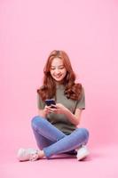 jonge aziatische vrouw zit en gebruikt smartphone op roze achtergrond foto