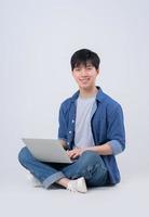jonge aziatische man zit en gebruikt laptop op witte achtergrond foto