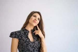 jonge vrouw met doordachte blik houdt vinger op haar kin, op witte achtergrond foto