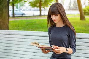mooie jonge vrouw zittend op een bankje in de straat een boek lezen foto