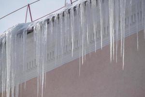 zicht op lange scherpe ijspegels die van het dak van het huis hangen. foto