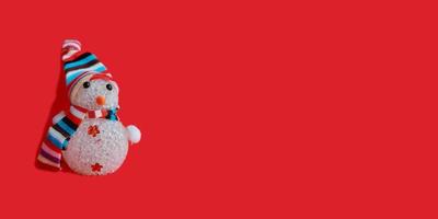 sneeuwpop in een gestreepte muts en sjaal op een rode achtergrond. kerstversiering banner, horizontaal, kopieer ruimte, plaats voor tekst. nieuwjaar, vakantie foto
