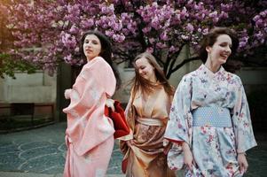 drie europese meisjes die traditionele japanse kimono dragen als achtergrond bloesem roze sakura boom foto