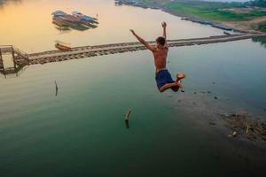 aziatische man springt van mon bridge in sangkhlaburi kanchanaburi bangkok thailand, beroemd springpunt van mon bridge sangkhlaburi, gevaarlijk springen in songgaria rivier foto