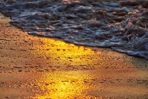 zonsondergang lichtreflectie op zeezandoppervlak, mooi geel zonlicht in zeeschuim, warm zandstrand foto