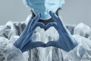 vrouw met medisch masker in onscherpte en handen in latexhandschoen toont het symbool van het hart. foto