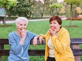 twee volwassen vrouwen die appels eten op de bank na het doen van sportoefeningen in het park. gezond levensstijlconcept foto